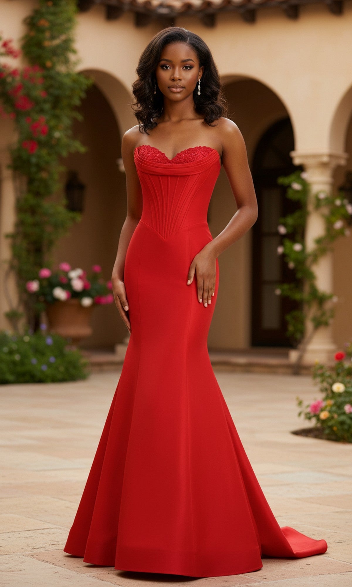 A woman stands outdoors in a courtyard with flowers and arches, wearing the fitted red Taffeta Mermaid Prom Dress: PromGirl Exclusive 250208, exuding elegance.